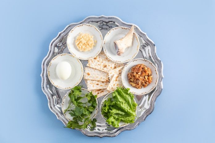 a silver plate with traditional Jewish treats for Passover. baked egg, lettuce, horseradish, bone, nuts and matzah. a symbol of the Jewish Passover.