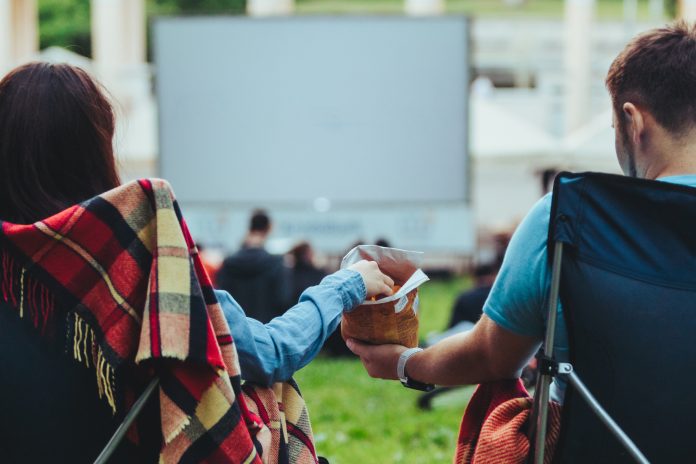 couple sitting in camp-chairs in city park looking movie outdoors at open air cinema